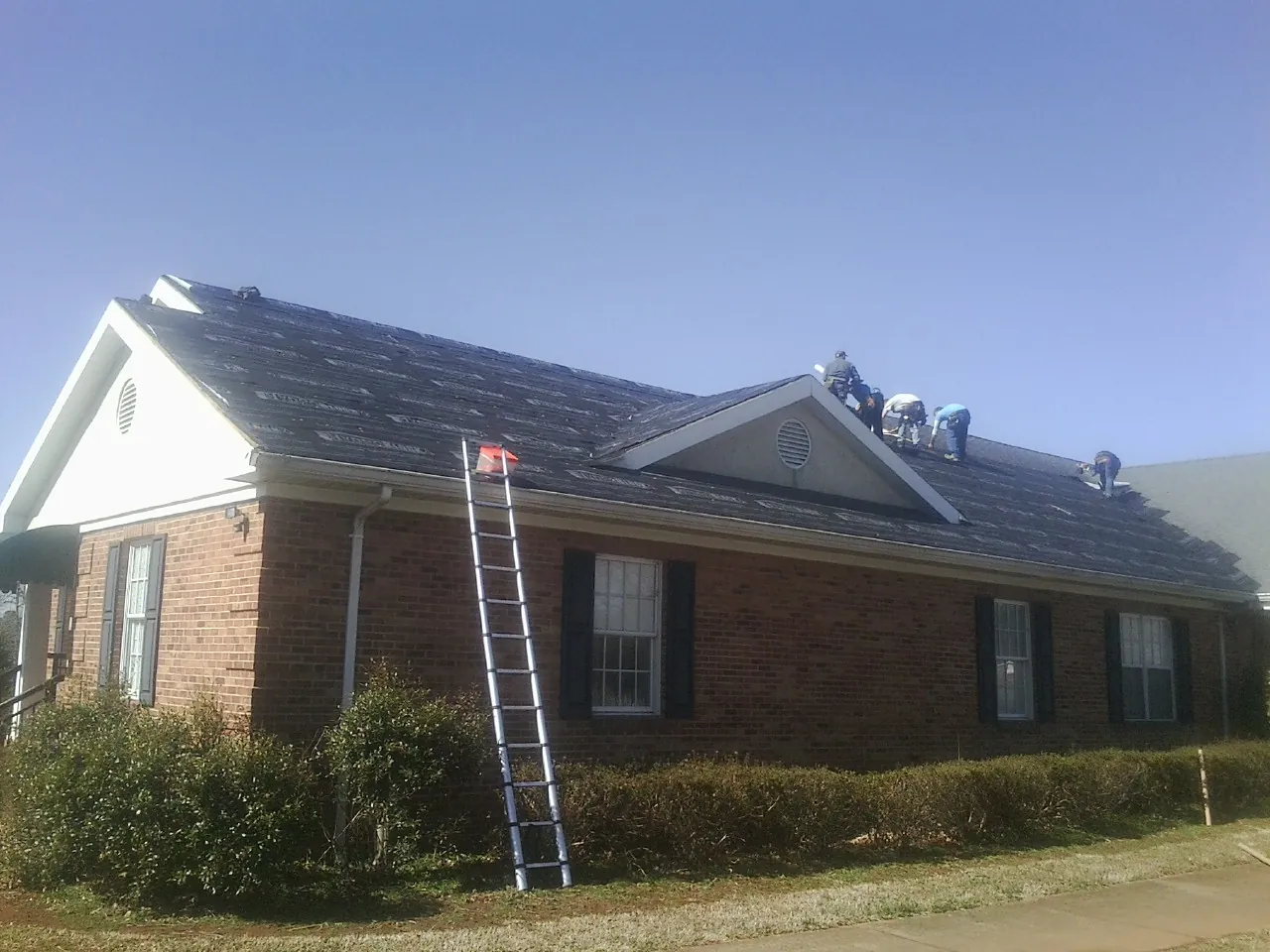 Crew tearing shingles off a brick ranch roof with a ladder set — Emergency Roof Repair work by our crew in Stockbridge