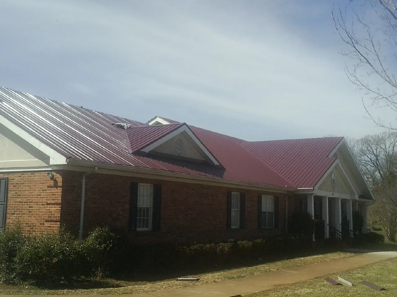 Red metal roof with gabled entries on a long brick building, from a Hail Damage Roof Repair job in Stockbridge